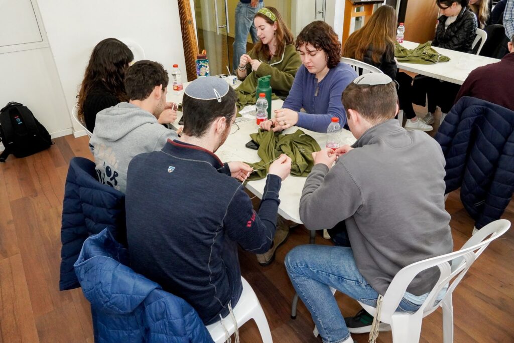 JLIC students weaving Tzitzit in IDF jerseys at Beit Eretz Hamada in Jan 2024 during the Winter Break Solidarity Israel Mission